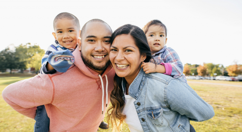 Smiling Latino/Hispanic family with two young children posing together outdoors.