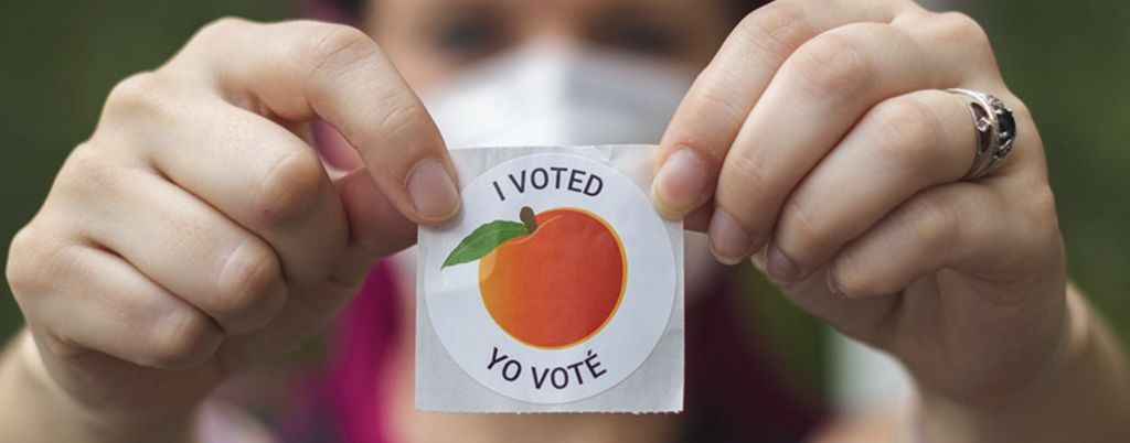 Woman holding up an “I voted/Yo voté” sticker with the famous Georgia peach.