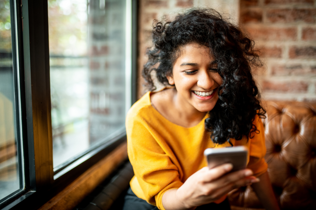 A Latina woman smiling at her phone outdoors, representing engagement with nonprofit social media content.